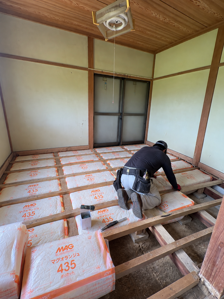 職人が床に断熱材を丁寧に敷き詰めている施工風景
